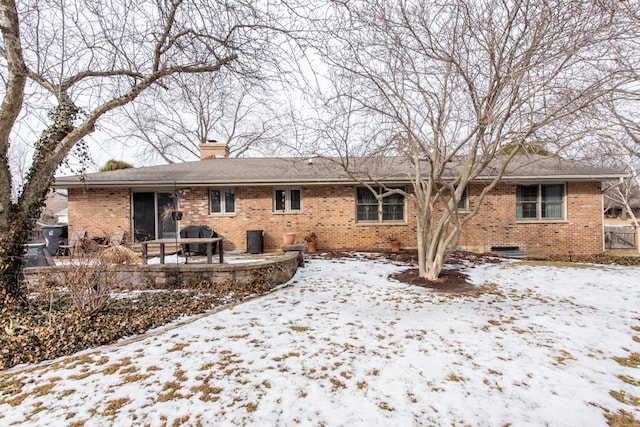 snow covered back of property with a patio area, brick siding, and a chimney