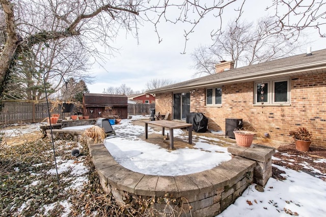 snow covered property with brick siding, a chimney, an outdoor structure, and a fenced backyard