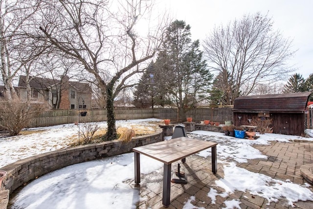 snow covered patio with an outbuilding, a storage unit, and a fenced backyard