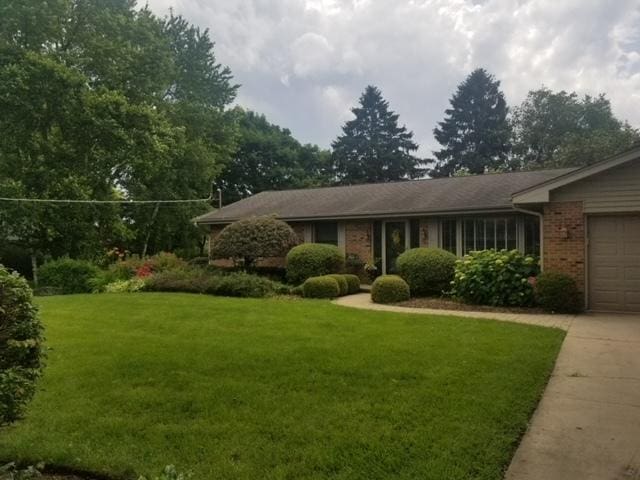 view of front of house featuring a front lawn, concrete driveway, brick siding, and an attached garage