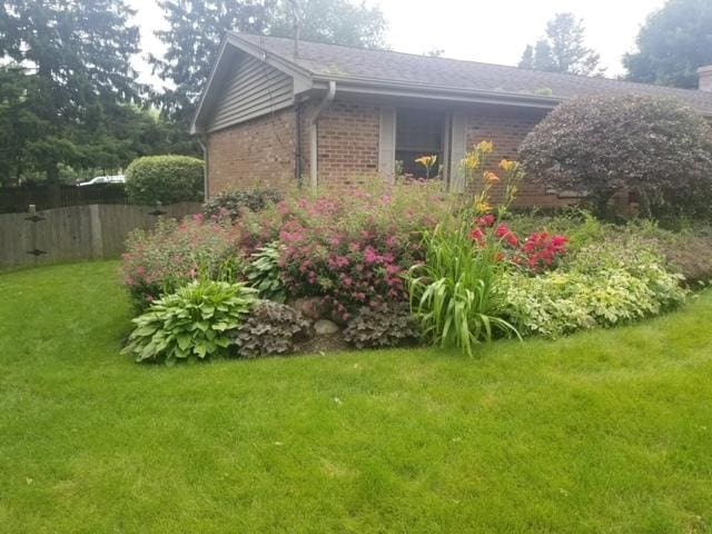 view of side of home featuring brick siding, a yard, and fence