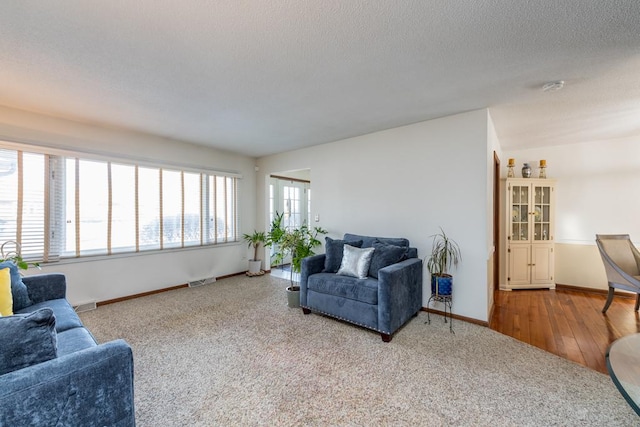 carpeted living room with a textured ceiling, baseboards, and wood finished floors