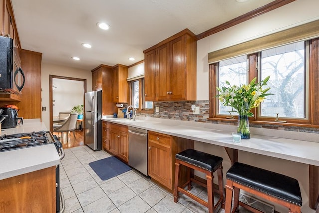 kitchen featuring light countertops, appliances with stainless steel finishes, a sink, and brown cabinets