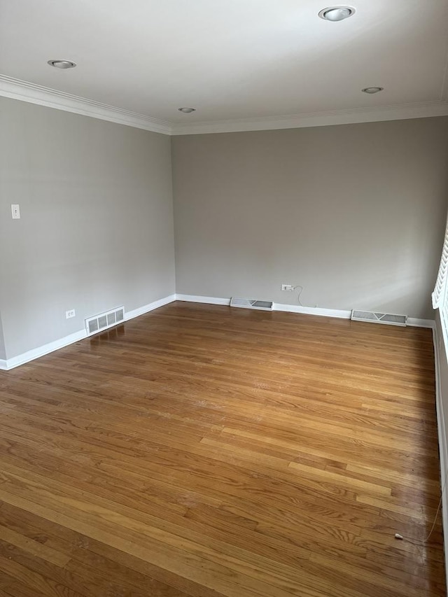 empty room featuring visible vents, wood finished floors, and ornamental molding