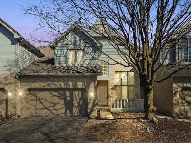 view of front of property featuring brick siding, driveway, a garage, and roof with shingles