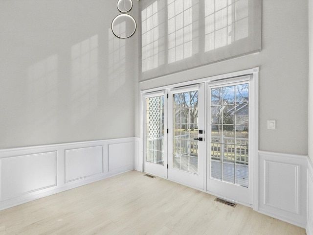 doorway featuring a wainscoted wall, a decorative wall, wood finished floors, and visible vents