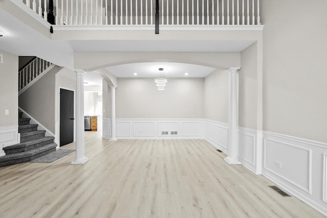 unfurnished room with visible vents, arched walkways, light wood-style floors, and ornate columns