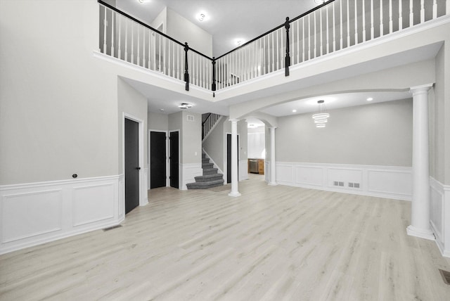 unfurnished living room with visible vents, wood finished floors, stairway, arched walkways, and decorative columns