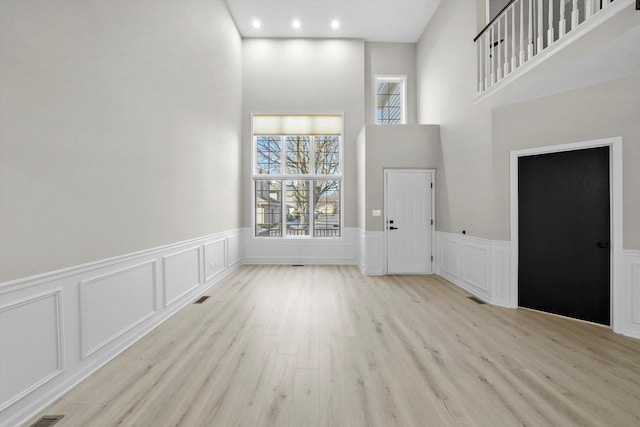 entrance foyer with visible vents, wood finished floors, recessed lighting, a decorative wall, and a towering ceiling