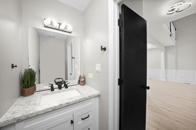 bathroom featuring a wainscoted wall, wood finished floors, vanity, and a decorative wall