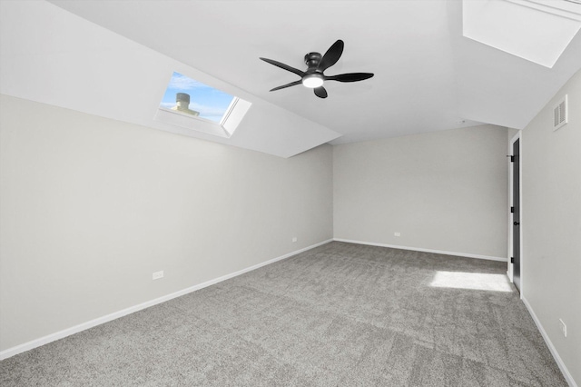 additional living space featuring a ceiling fan, visible vents, baseboards, vaulted ceiling with skylight, and carpet flooring