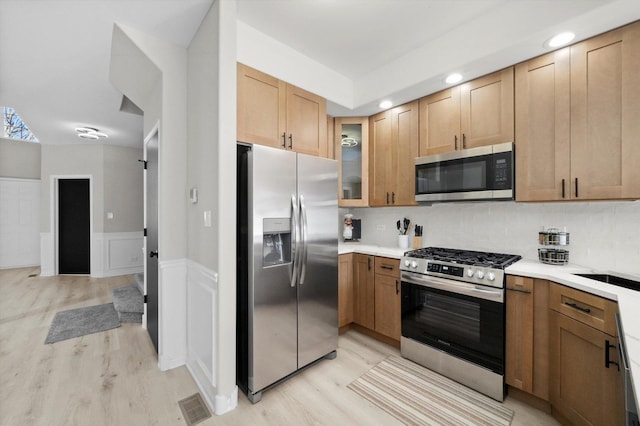 kitchen with visible vents, glass insert cabinets, light wood-type flooring, wainscoting, and stainless steel appliances