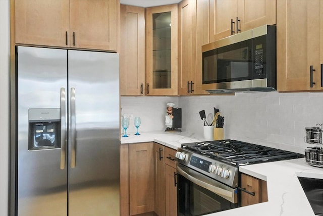 kitchen featuring light stone counters, glass insert cabinets, tasteful backsplash, and appliances with stainless steel finishes