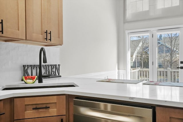 kitchen featuring brown cabinets, a sink, light stone counters, stainless steel dishwasher, and decorative backsplash