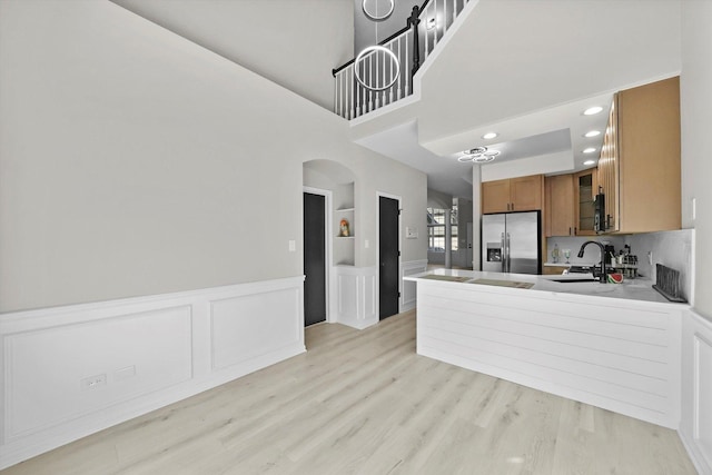 kitchen featuring light wood-style flooring, arched walkways, a sink, stainless steel fridge, and brown cabinets