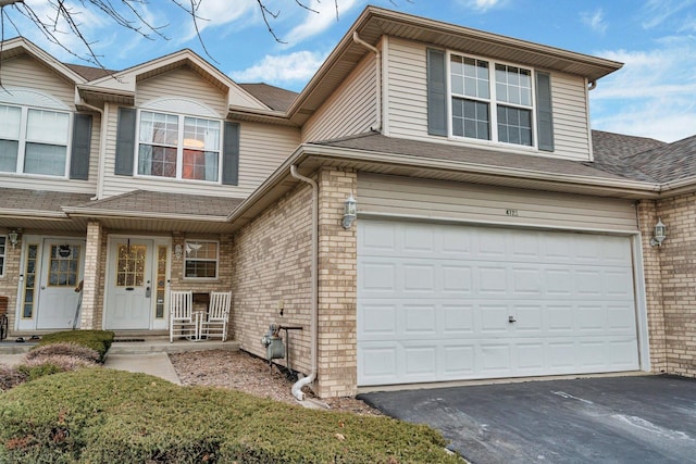 view of front of property with an attached garage, a shingled roof, aphalt driveway, and brick siding