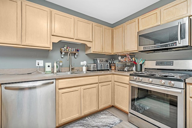 kitchen with light countertops, appliances with stainless steel finishes, a sink, and light brown cabinetry