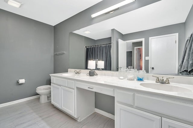 full bathroom featuring double vanity, a sink, toilet, and baseboards