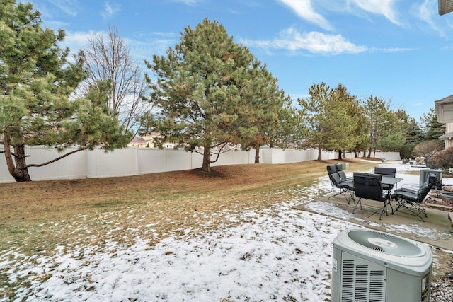 yard layered in snow featuring a patio area, a fenced backyard, and central air condition unit