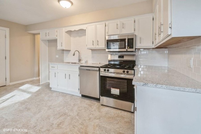 kitchen featuring stainless steel appliances, white cabinetry, backsplash, and light stone countertops