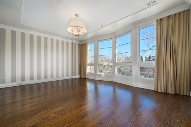 unfurnished room with a notable chandelier, dark wood-type flooring, visible vents, baseboards, and wallpapered walls