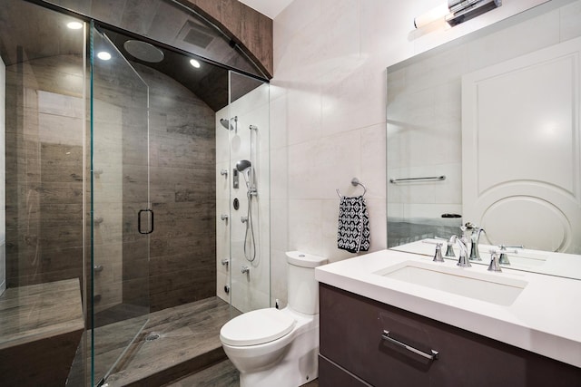 bathroom with tile walls, a shower stall, toilet, and vanity