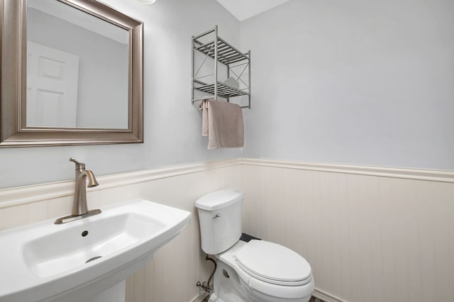 half bath with a wainscoted wall, a sink, and toilet