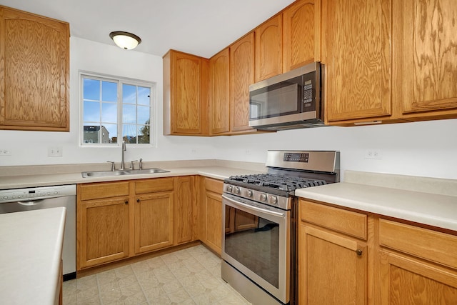 kitchen featuring stainless steel appliances, a sink, light countertops, brown cabinets, and light floors