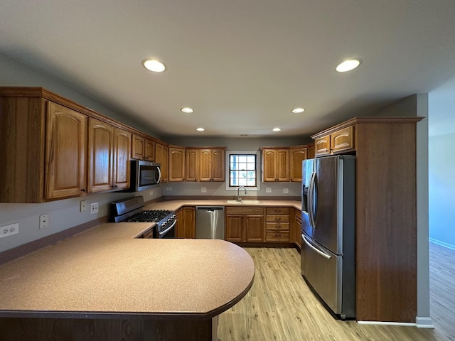 kitchen featuring appliances with stainless steel finishes, brown cabinets, a peninsula, light countertops, and a sink