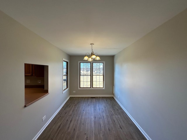 unfurnished dining area featuring dark wood-style flooring, baseboards, and an inviting chandelier