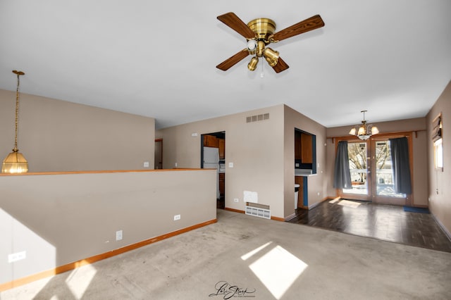 unfurnished living room featuring carpet, visible vents, baseboards, and ceiling fan with notable chandelier