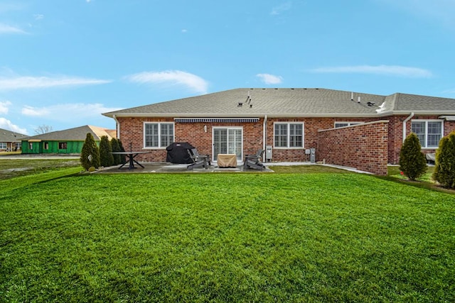 back of property with a shingled roof, a patio area, brick siding, and a lawn