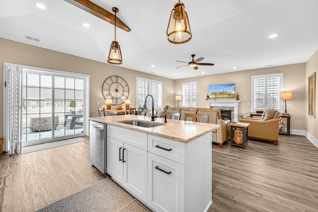 kitchen with a sink, light wood-style floors, lofted ceiling with beams, and stainless steel dishwasher