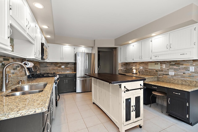 kitchen with stainless steel appliances, light tile patterned flooring, a sink, and white cabinetry