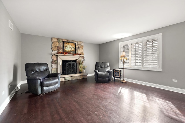 living area featuring visible vents, a stone fireplace, baseboards, and wood finished floors