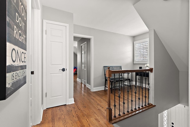 hall with an upstairs landing, baseboards, and wood finished floors