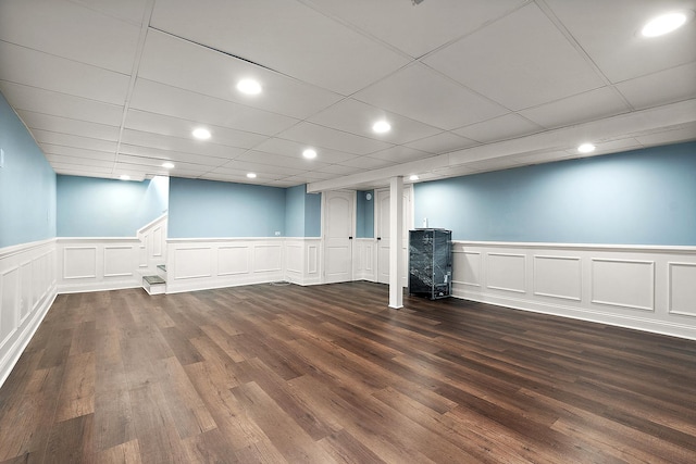 finished below grade area with a wainscoted wall, a drop ceiling, dark wood finished floors, and recessed lighting