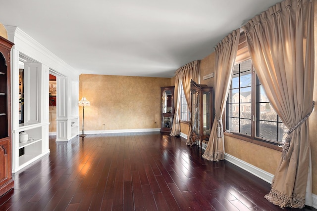 unfurnished living room featuring wood-type flooring, baseboards, and ornate columns