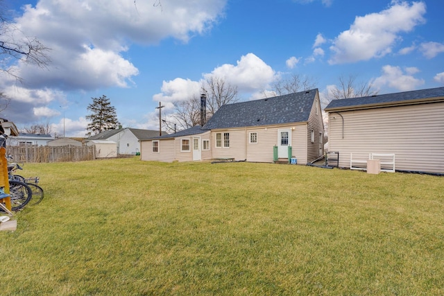 back of house featuring a shingled roof, a lawn, and fence