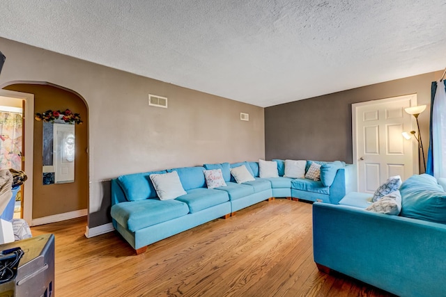 living room featuring arched walkways, a textured ceiling, light wood-type flooring, and visible vents