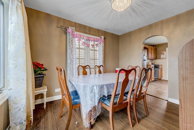 dining space featuring arched walkways, light wood-style flooring, and baseboards