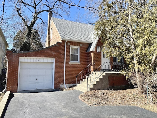 view of front of home with aphalt driveway, a garage, brick siding, a shingled roof, and a chimney