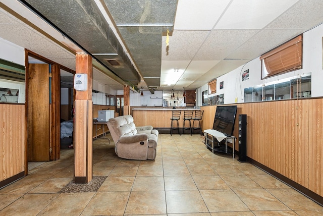 basement with a paneled ceiling, visible vents, wainscoting, wood walls, and tile patterned floors