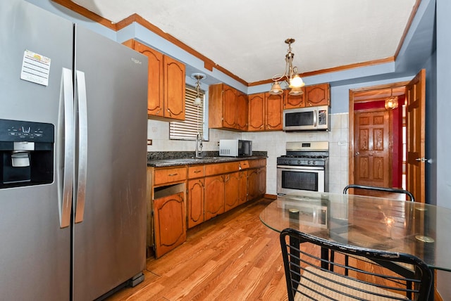 kitchen with brown cabinets, decorative light fixtures, stainless steel appliances, light wood-style floors, and a sink