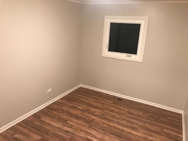 empty room featuring dark wood-style flooring, visible vents, and baseboards