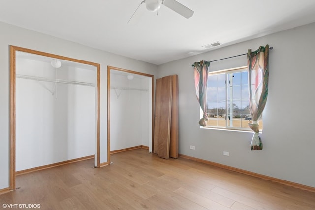 unfurnished bedroom featuring baseboards, visible vents, ceiling fan, light wood-type flooring, and two closets