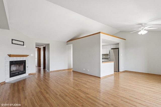 unfurnished living room featuring a ceiling fan, light wood finished floors, baseboards, vaulted ceiling, and a tile fireplace