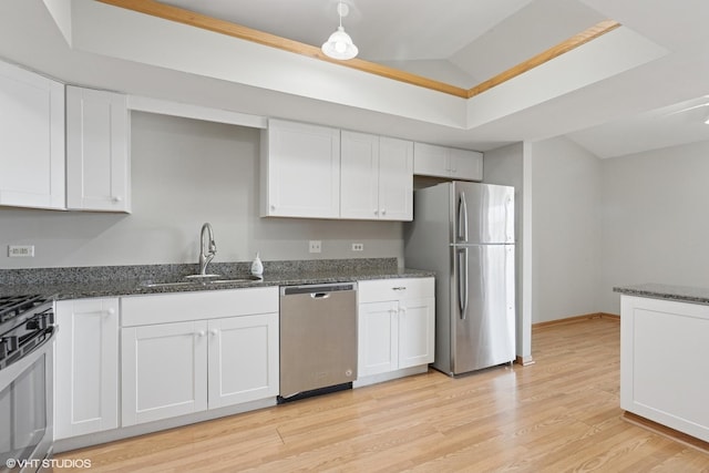 kitchen featuring a sink, dark stone counters, appliances with stainless steel finishes, white cabinets, and light wood finished floors