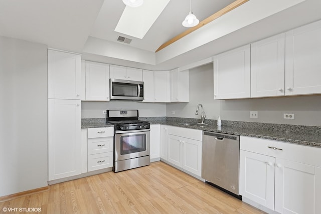 kitchen featuring light wood-type flooring, appliances with stainless steel finishes, a skylight, white cabinets, and a sink