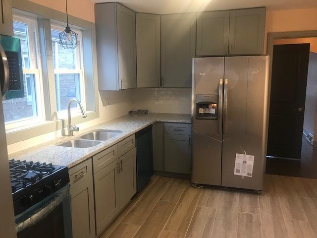 kitchen featuring light wood finished floors, decorative light fixtures, gray cabinets, stainless steel appliances, and a sink